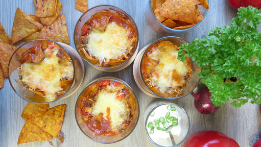 4 Meal Prep Gläser, gefüllt mit TexMex Hackfleisch und Nachos, ein Glas mit Dip, rechts Petersilie